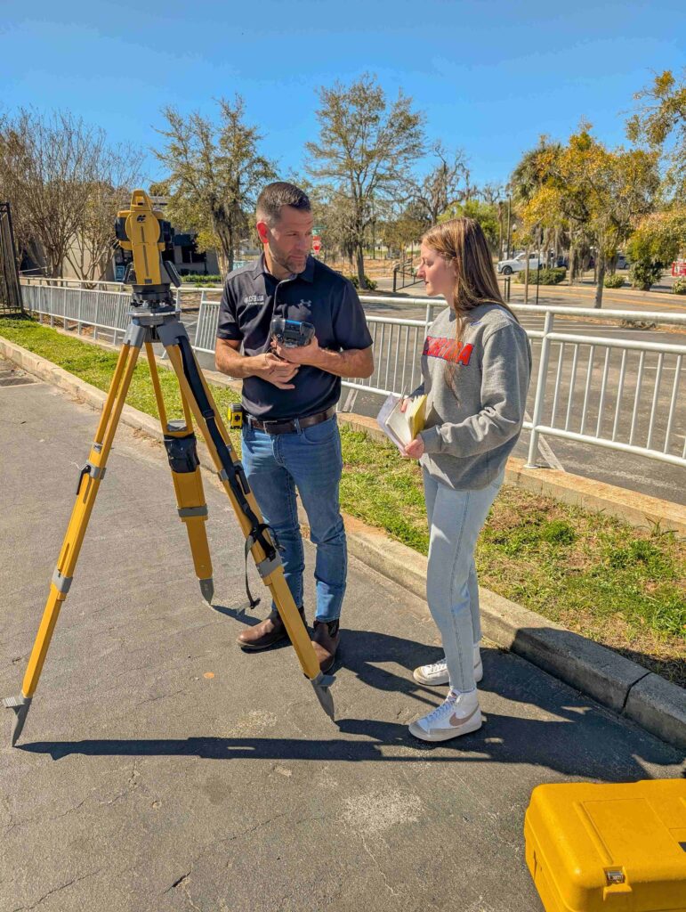 Jeremy Hallick, PSM demonstrates surveying instrument while UF geomatics student looks on.