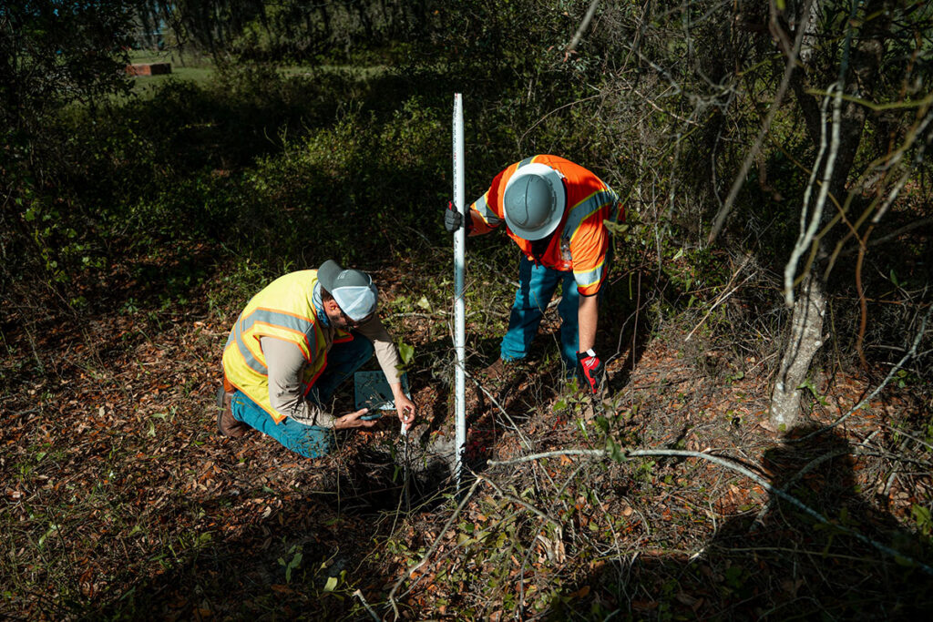 CFB Surveying SUE crew measuring depth with survey rod in wooded area